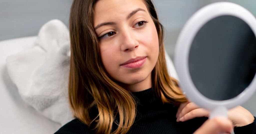young woman looking at her face in mirror after starting Accutane treatment