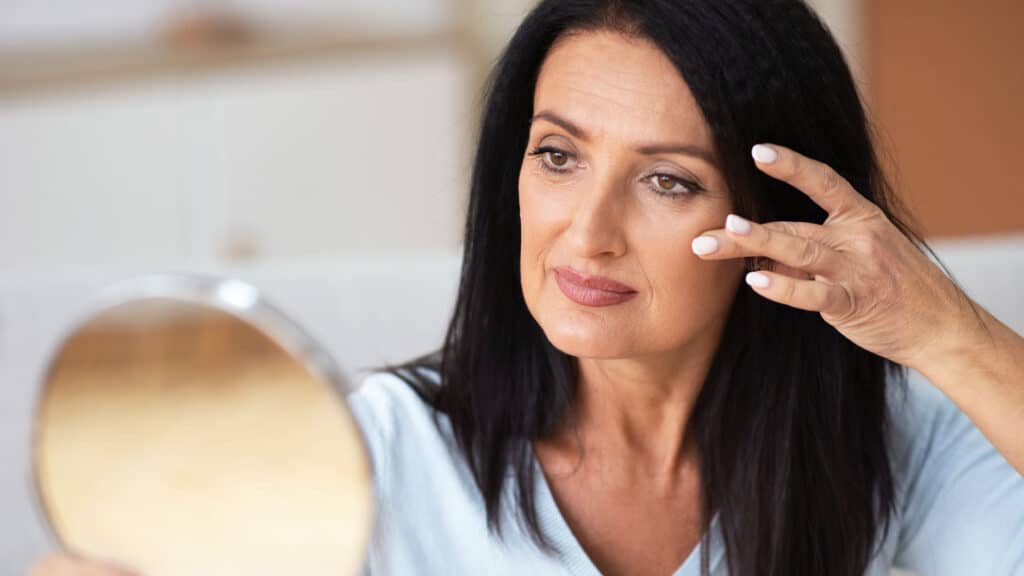 Older woman examining her skin in the mirror before fluorouracil treatment