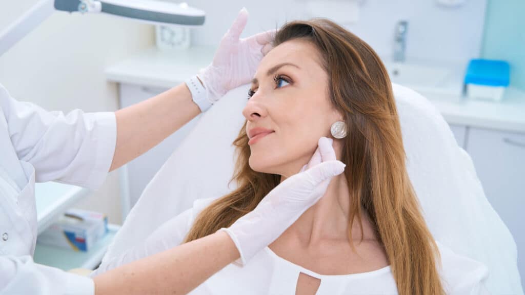 Dermatologist consulting with a woman as she examines her skin in a mirror during a skin health evaluation.
