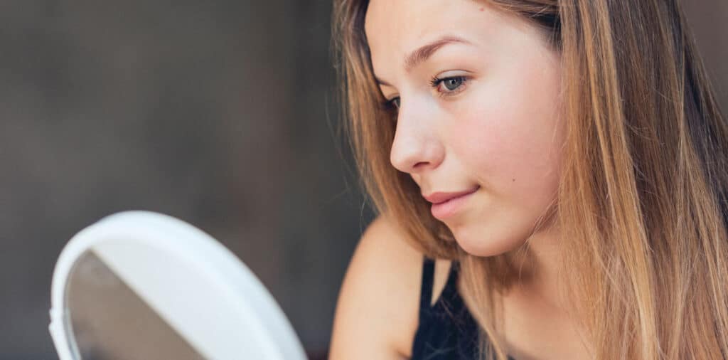 Young woman examining acne on her face in a mirror.