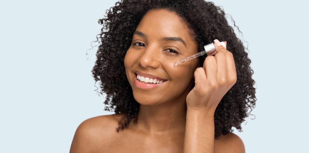 Woman applying facial serum to her cheek with a dropper as part of her skincare routine.
