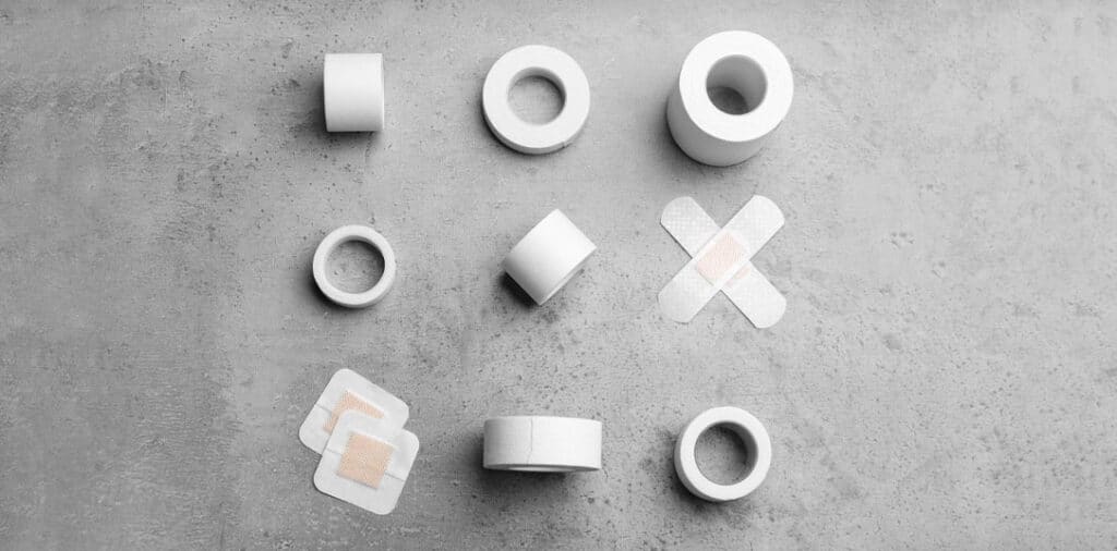 Various types of medical tape and adhesive bandages arranged on a gray surface for wound care.