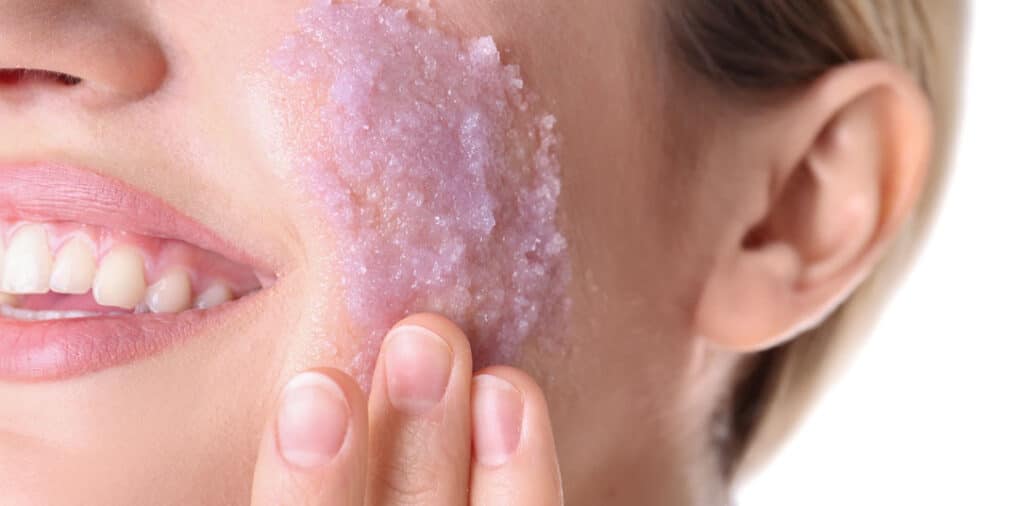 Close-up of a woman applying an exfoliating facial scrub to her cheek.